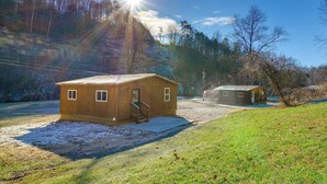 A wooden cabin with a porch and a smaller adjacent building, surrounded by a snowy landscape and trees. - Peaceful Beattyville Cabin Near Red River Gorge! (Beattyville)