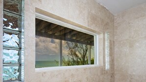 Ein Badezimmer mit großem Fenster, einer Dusche und Blick ins Freie.