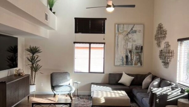 Un salon moderne avec un canapé, un fauteuil et une table basse, un ventilateur de plafond et un grand tableau abstrait accroché au mur.