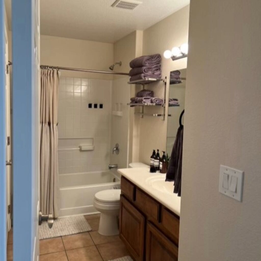 A bathroom with a shower, toilet, and vanity. There are towels and toiletries on the vanity.