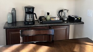 Une cuisine avec des meubles de rangement en bois, un plan de travail sur lequel se trouvent une machine à café, une bouilloire et une tasse.