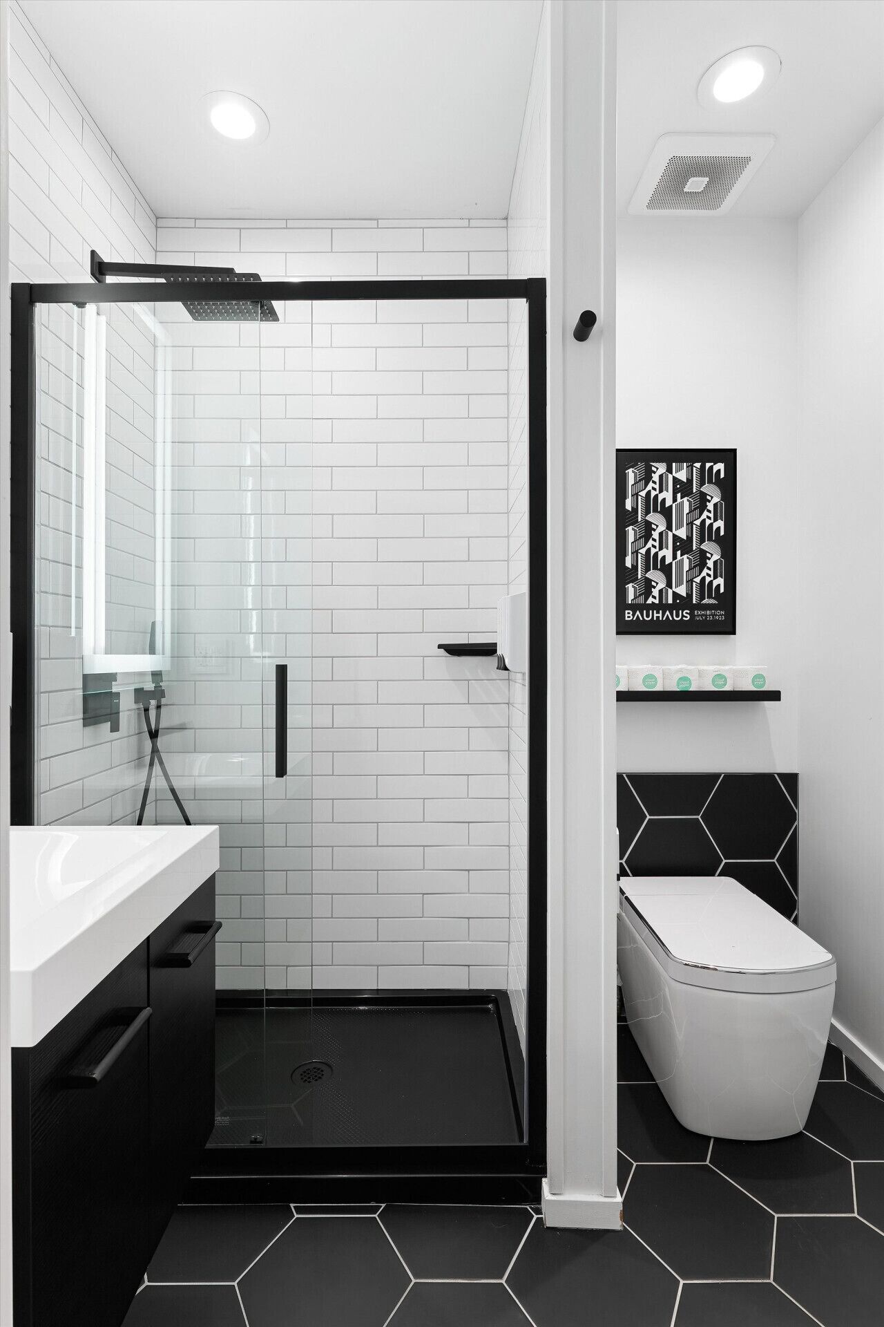 A modern bathroom with white subway tiles, a glass shower enclosure, a black sink, and a toilet.
