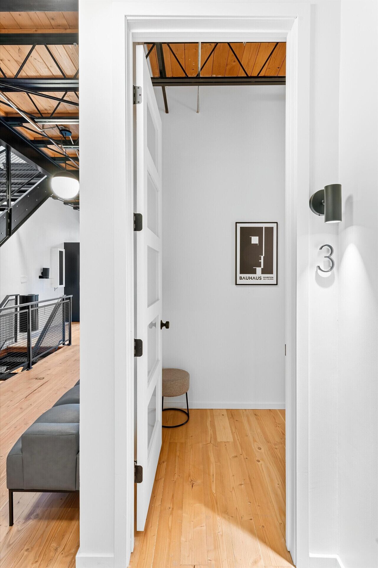 Ein modernes Interieur mit einer Treppe, einem gerahmten Schild einer Bauhaus-Ausstellung und der Zahl '3' an der Wand.
