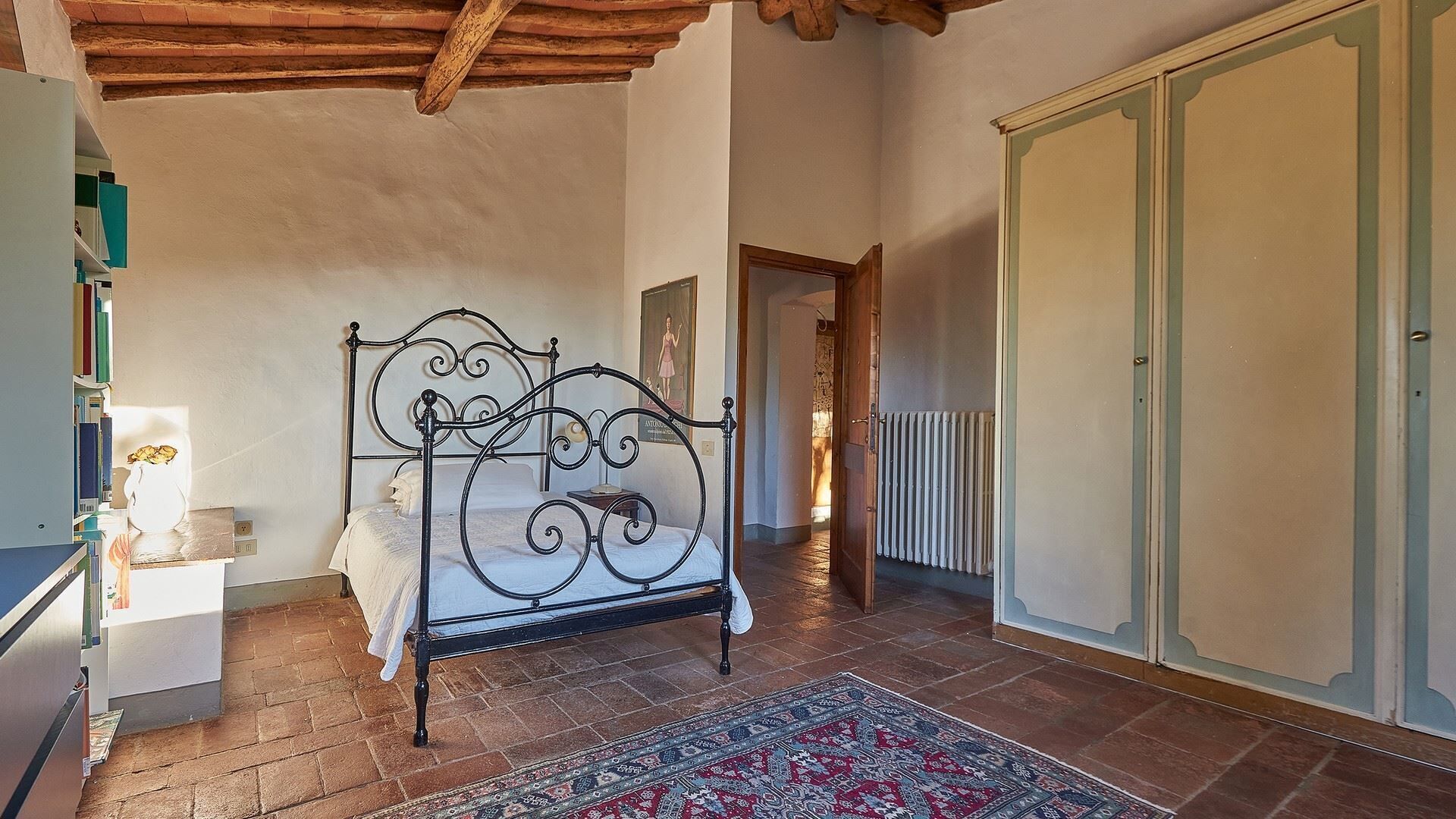 A bedroom with a metal bed frame, a radiator, a wardrobe, and a patterned rug.
