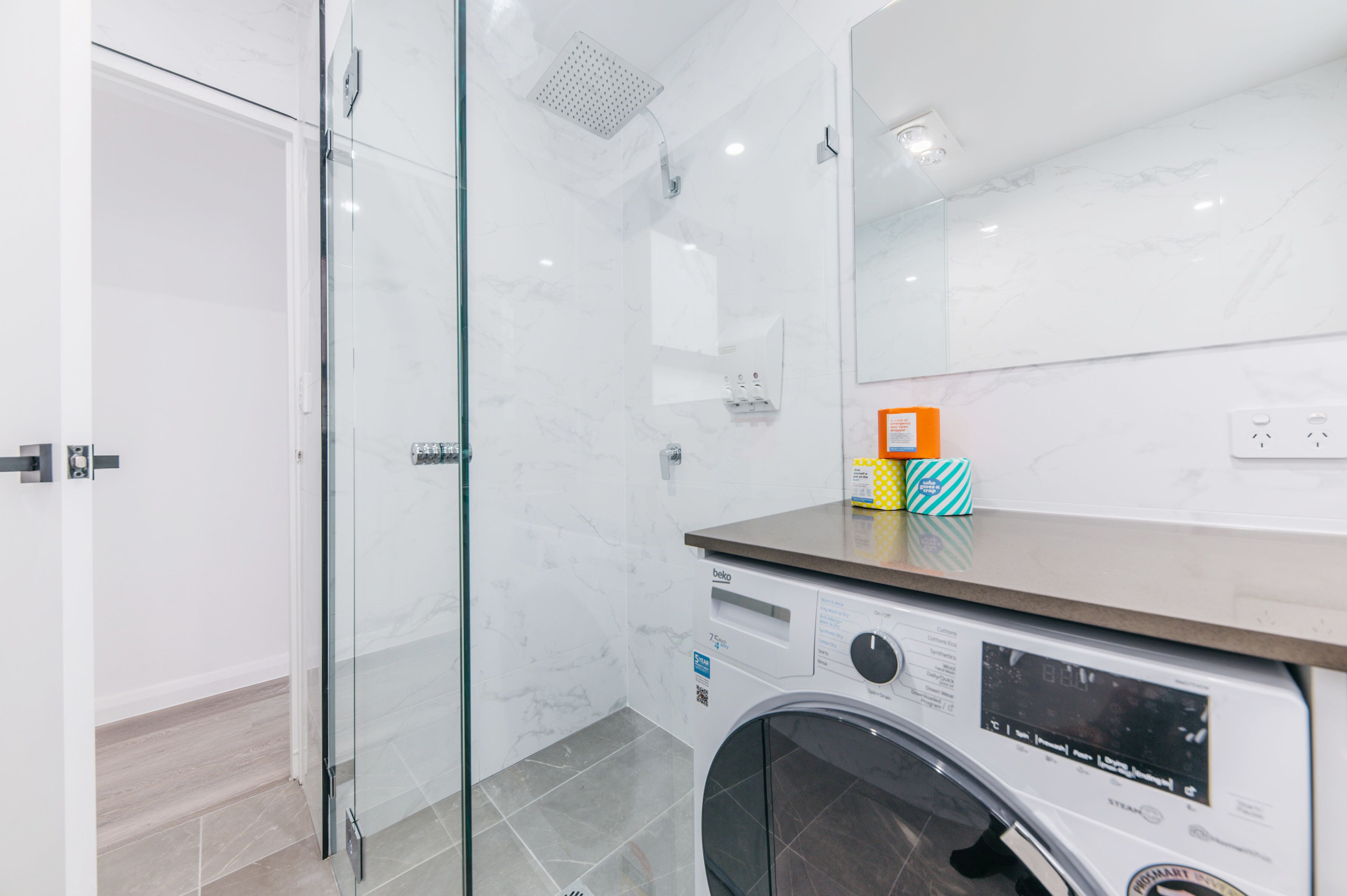 Un baño moderno con cabina de ducha de vidrio, lavadora integrada y un espejo grande.