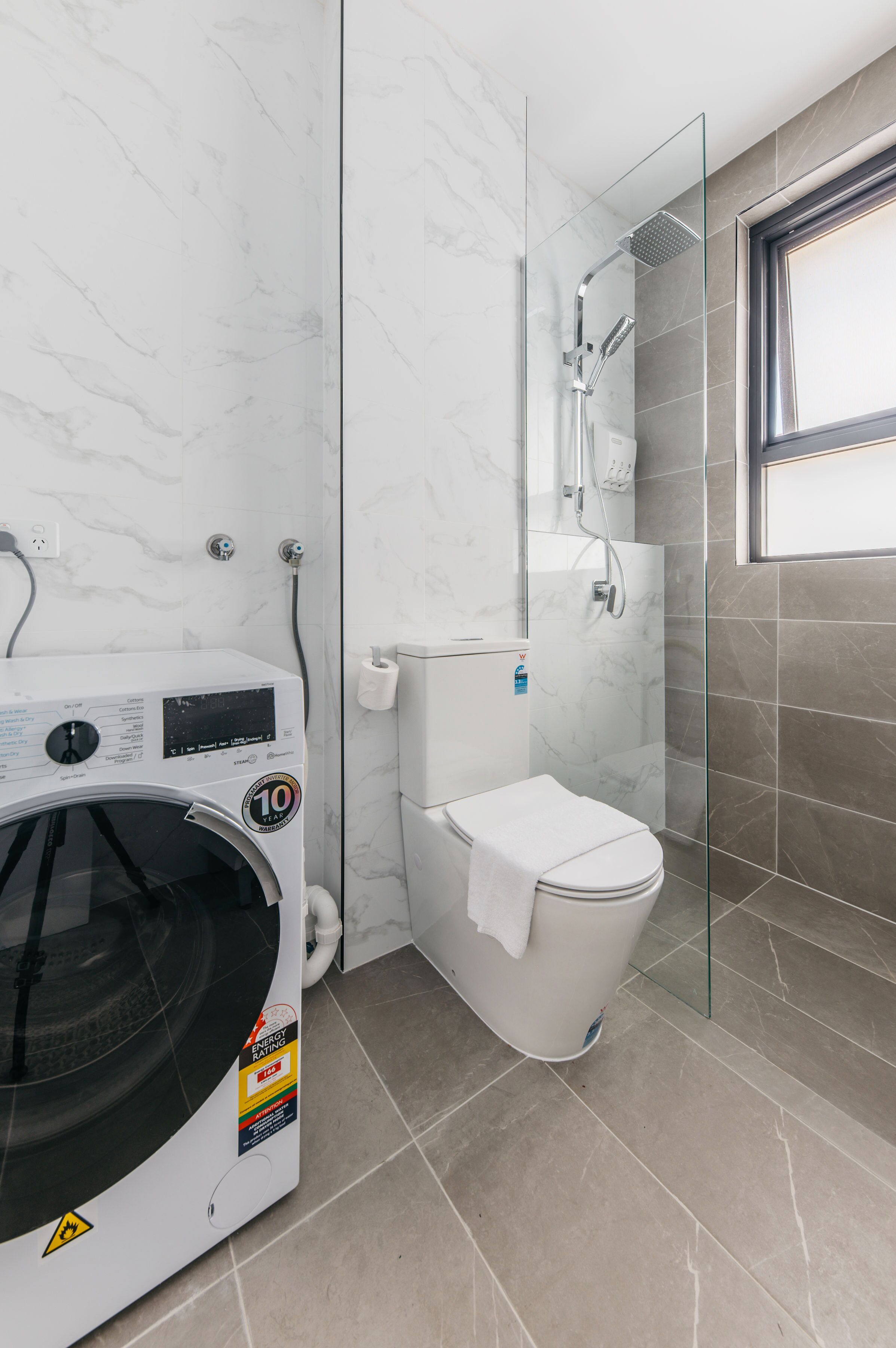 Een compacte badkamer met een glazen douchecabine, een wit toilet en een voorlader wasmachine.