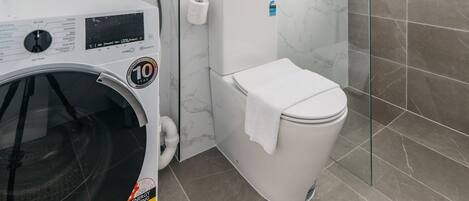 A compact bathroom with a glass shower enclosure, a white toilet, and a front-loading washing machine.