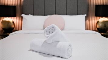 A neatly made bed with a rolled white towel in the center, a white pillow, and a pink pillow on the headboard.