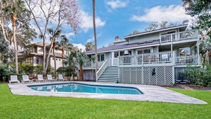 Una casa de dos pisos con piscina, un patio cubierto y un césped bien cuidado.