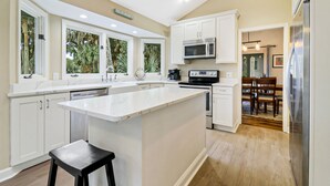 Una cocina moderna con una isla grande, armarios blancos y vistas a un comedor.