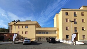 A multi-story building with a flat facade, several windows, and a parking area in front. - AH Roma (Rome)