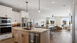 A modern kitchen with built-in appliances, a large island, and a dining area with a view. - Rock Creek At Desert Color 5 Bedroom Townhouse (St. George)