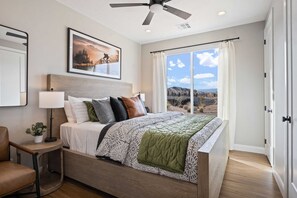 Relax in this serene bedroom with a large bed, ceiling fan, and picture above, offering a view of the outdoors through sheer curtains.
