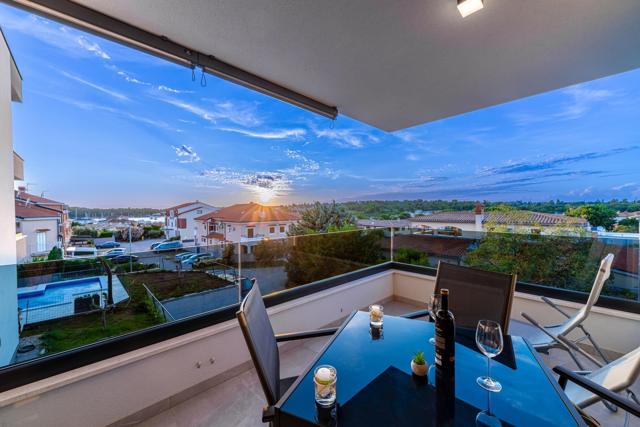Un balcon avec une table dressée pour deux personnes, donnant sur un quartier résidentiel avec des maisons et un ciel dégagé.