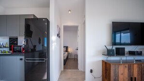 Una cuina moderna amb un frigorífic negre, un microones i una cafetera. Hi ha un armari de fusta amb un televisor de pantalla plana a sobre.