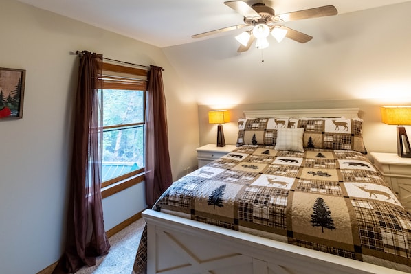 A bedroom with a quilted bedspread featuring animal prints, a ceiling fan, bedside lamps, and a window with curtains. - Hot Tub - Views - Gas Firepit (Bryson City)