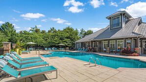 A pool area with lounge chairs, a covered seating area, and a building with a large window and a tower. - Fast WiFi, King Bed, Gym w/ Free Parking (Huntsville)