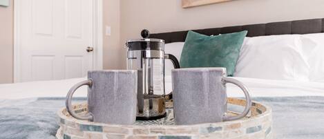 Una cama con una bandeja metálica que sostiene dos tazas y una cafetera.