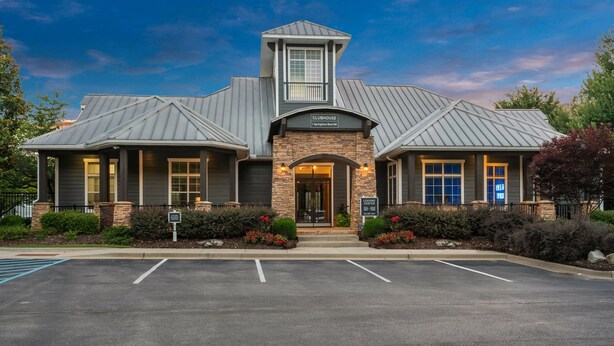 A two-story clubhouse with a prominent entrance, a parking lot in front, and a sign indicating it is a leasing center. - Fast WiFi, King Bed, Gym w/ Free Parking (Huntsville)
