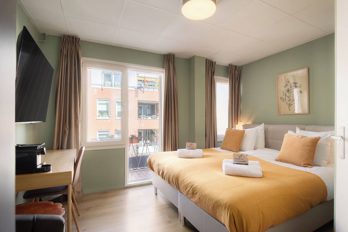 Une chambre d’hôtel avec un lit, un bureau, une chaise, une télévision et une fenêtre avec des rideaux.