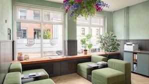 A modern kitchen with green upholstered seating, large windows, and a hanging plant.