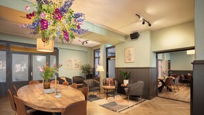 A modern dining area with a wooden table, brown chairs, a hanging floral arrangement, and a large window.