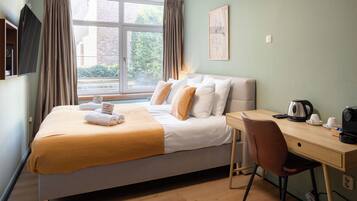 A hotel room with a bed, a desk, a chair, a window with curtains, a flat-screen TV, and a framed picture on the wall.