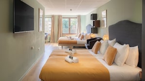 A hotel room with a large bed, a television, a balcony view, and a desk with a lamp.