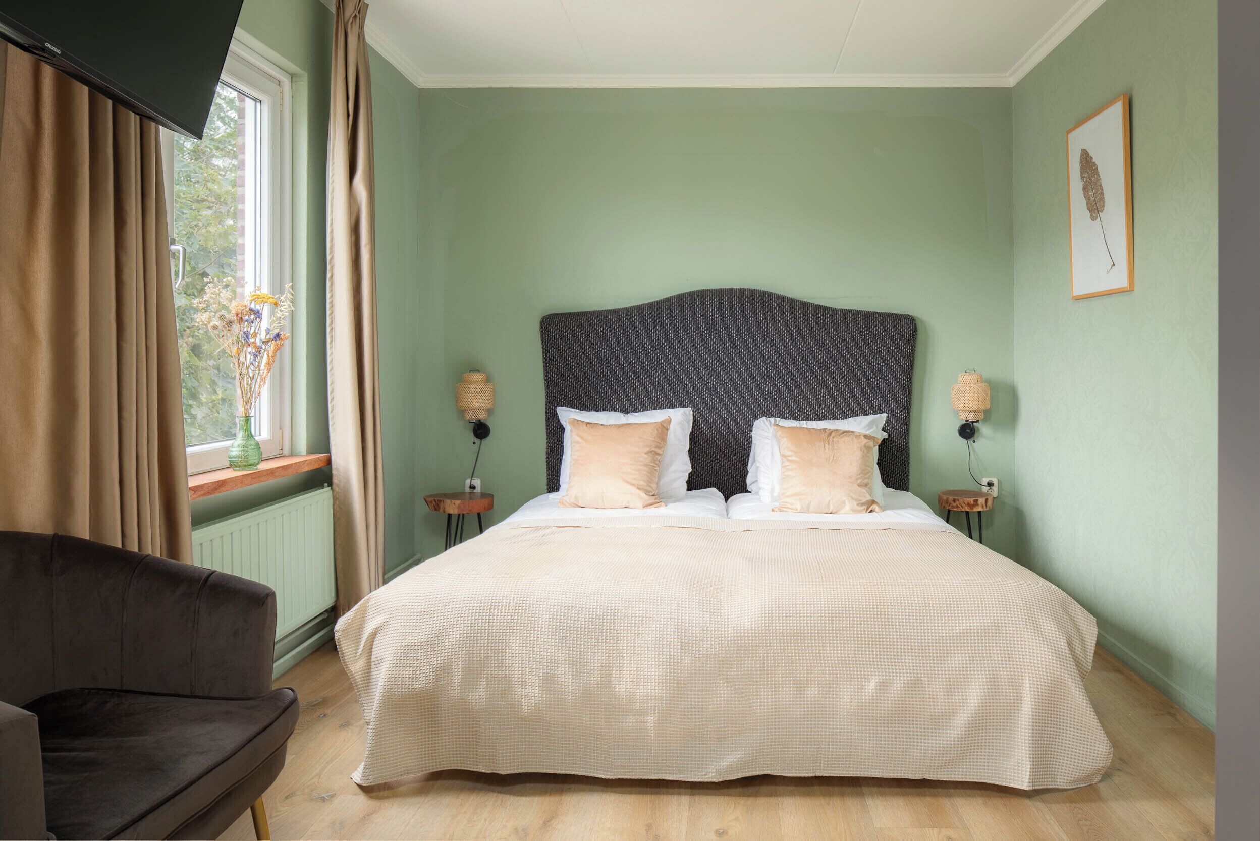 A bedroom with a large bed, two bedside tables, a chair, and a window with curtains.