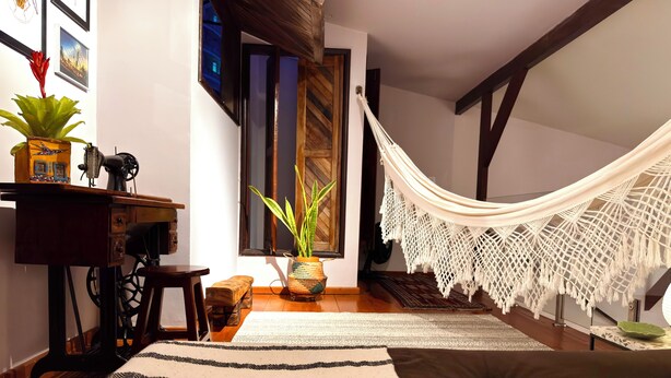A cozy room with a hammock, a sewing machine, a wooden desk, a potted plant, and a striped rug. - Casa Felicidade, sua Estadia Perfeita em Belém! (Belém)