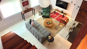 A modern living room with a grey sofa, a coffee table, and a TV. There are decorative items on the coffee table and a red rug on the floor. - Casa Felicidade, sua Estadia Perfeita em Belém! (Belém)