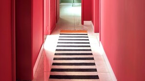 A hallway with red walls, a black and white striped rug, and a door leading to a room with a green wall and a lamp. - Casa Felicidade, sua Estadia Perfeita em Belém! (Belém)