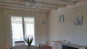 A dining area with a table, chairs, a sofa, and a kitchen area with cabinets and a countertop. - Maison Chaleureuse Entièrement Clôturée Animaux Acceptés (Le Poinçonnet)