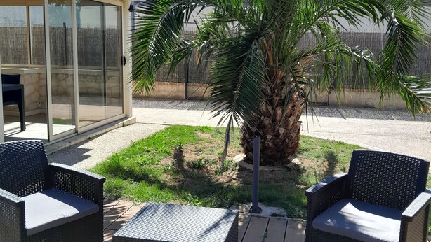 A patio with wicker furniture, a palm tree, and a covered seating area. - Maison Chaleureuse Entièrement Clôturée Animaux Acceptés (Le Poinçonnet)