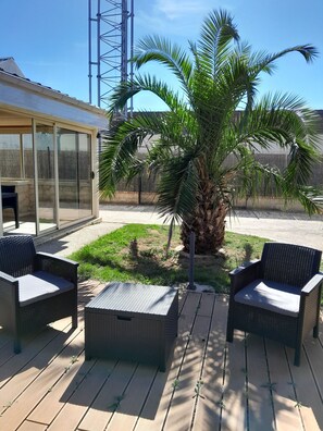 A patio with wicker furniture, a palm tree, and a covered seating area. - Maison Chaleureuse Entièrement Clôturée Animaux Acceptés (Le Poinçonnet)