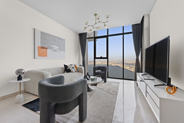 A modern living room with a sofa, armchairs, a coffee table, a flat-screen TV, and a large window with a view.
