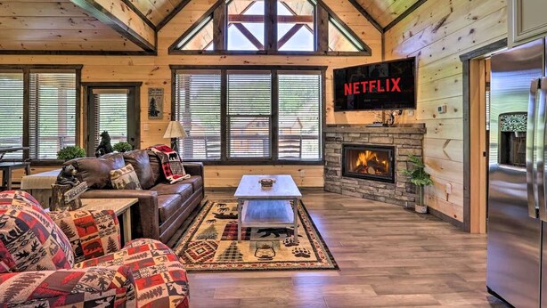A cozy living room with a fireplace, a television mounted on the wall, and a stone fireplace. - Wanderlust Pool Cabin: Private Pool, Hot Tub (Sevierville)