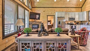 A cozy cabin interior with a wooden ceiling, a fireplace, a television, and a kitchen area. - Wanderlust Pool Cabin: Private Pool, Hot Tub (Sevierville)
