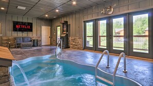 An indoor swimming pool with a stone wall and a Netflix screen. - Wanderlust Pool Cabin: Private Pool, Hot Tub (Sevierville)