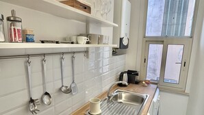 Una cocina moderna con estantes blancos, una placa de inducción negra y un ventanal con persianas.
