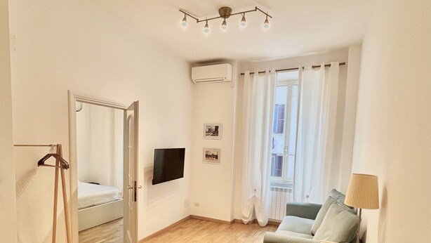 Un espacio habitable amplio con piso de madera, un sofá verde, una mesita con una lámpara, un televisor montado en la pared y una decoración en forma de estrella en el piso.