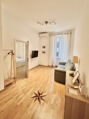 Un vaste espace de vie doté d’un plancher en bois, d’un canapé vert, d’une petite table avec une lampe, d’un téléviseur fixé au mur et d’un élément de d écoration en forme d’étoile posé sur le sol.