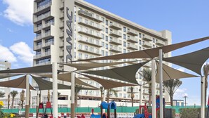 A modern building with balconies and a playground area with slides and a small train set.