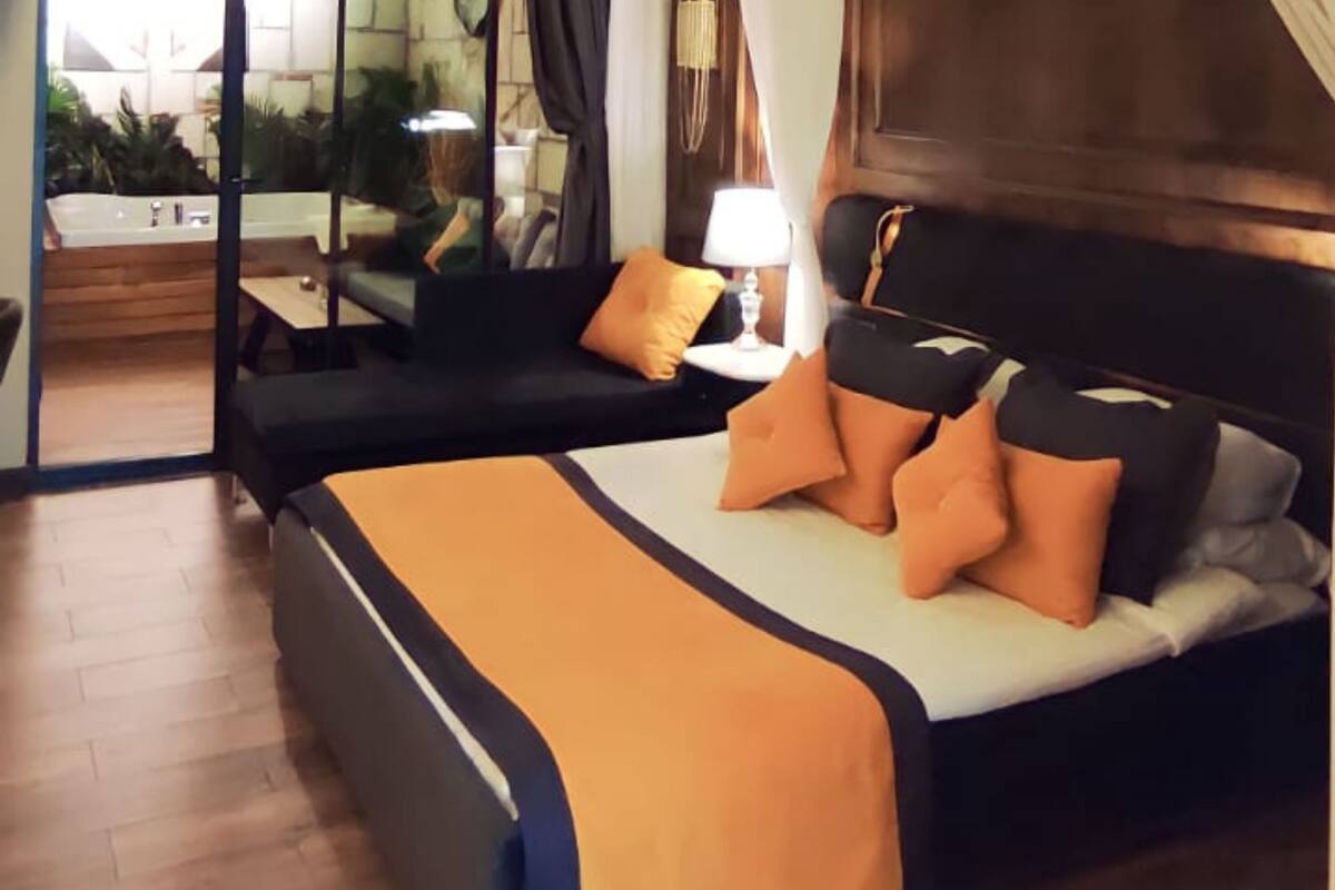 A hotel room with a bed, a sofa, a lamp, and a view of a garden.