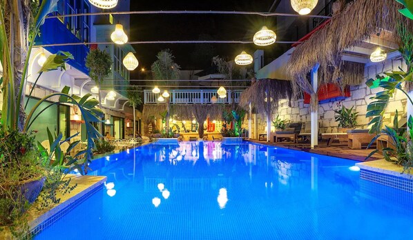 Una piscina interior con superficie de agua azul cristalina, rodeada de sillas de descanso y plantas en macetas.