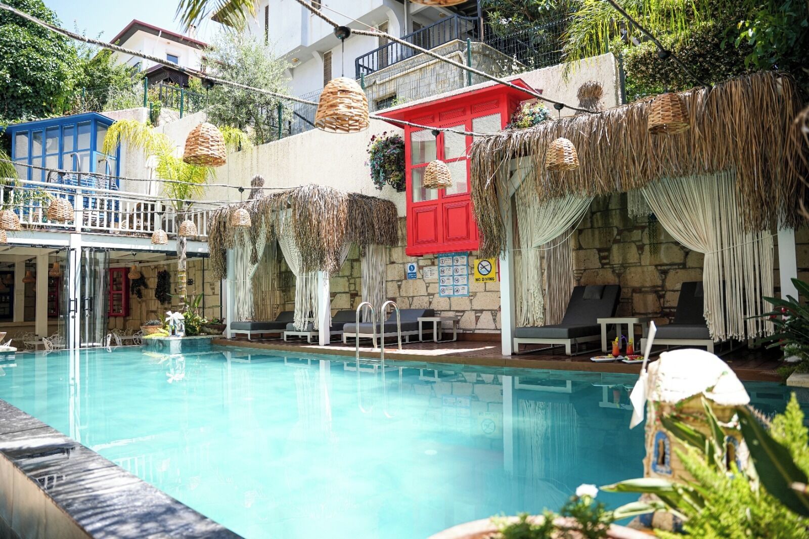 A swimming pool with lounge chairs, a red building, and hanging baskets.