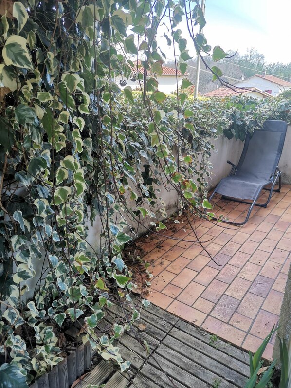 A patio area with a tiled floor, a wooden deck, and a chair. - T2 Lumineux Avec Jardinet - Barbotan les Thermes (Barbotan les Thermes)