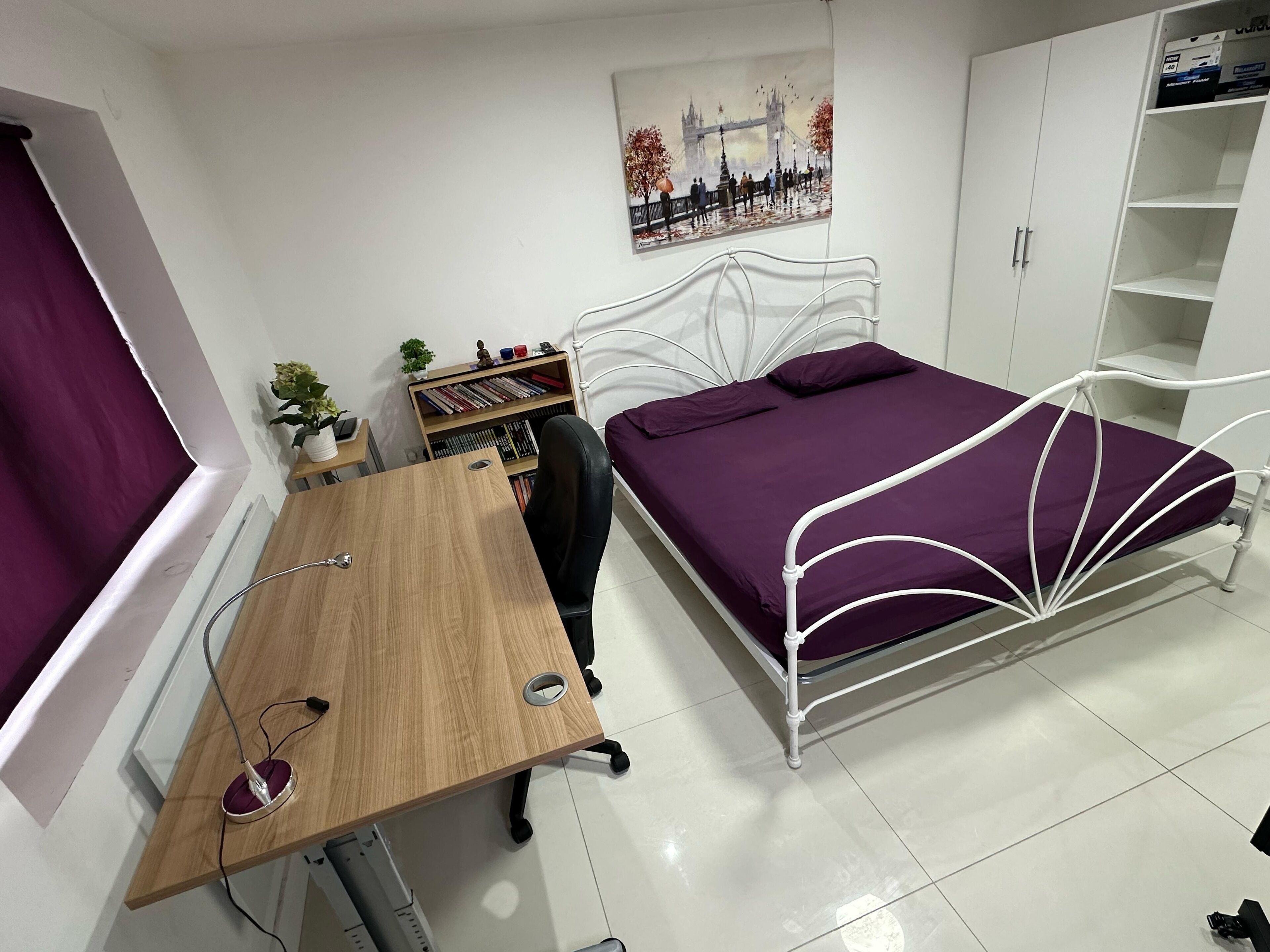 A bedroom with a bed, a desk, a chair, a bookshelf, and a painting on the wall.