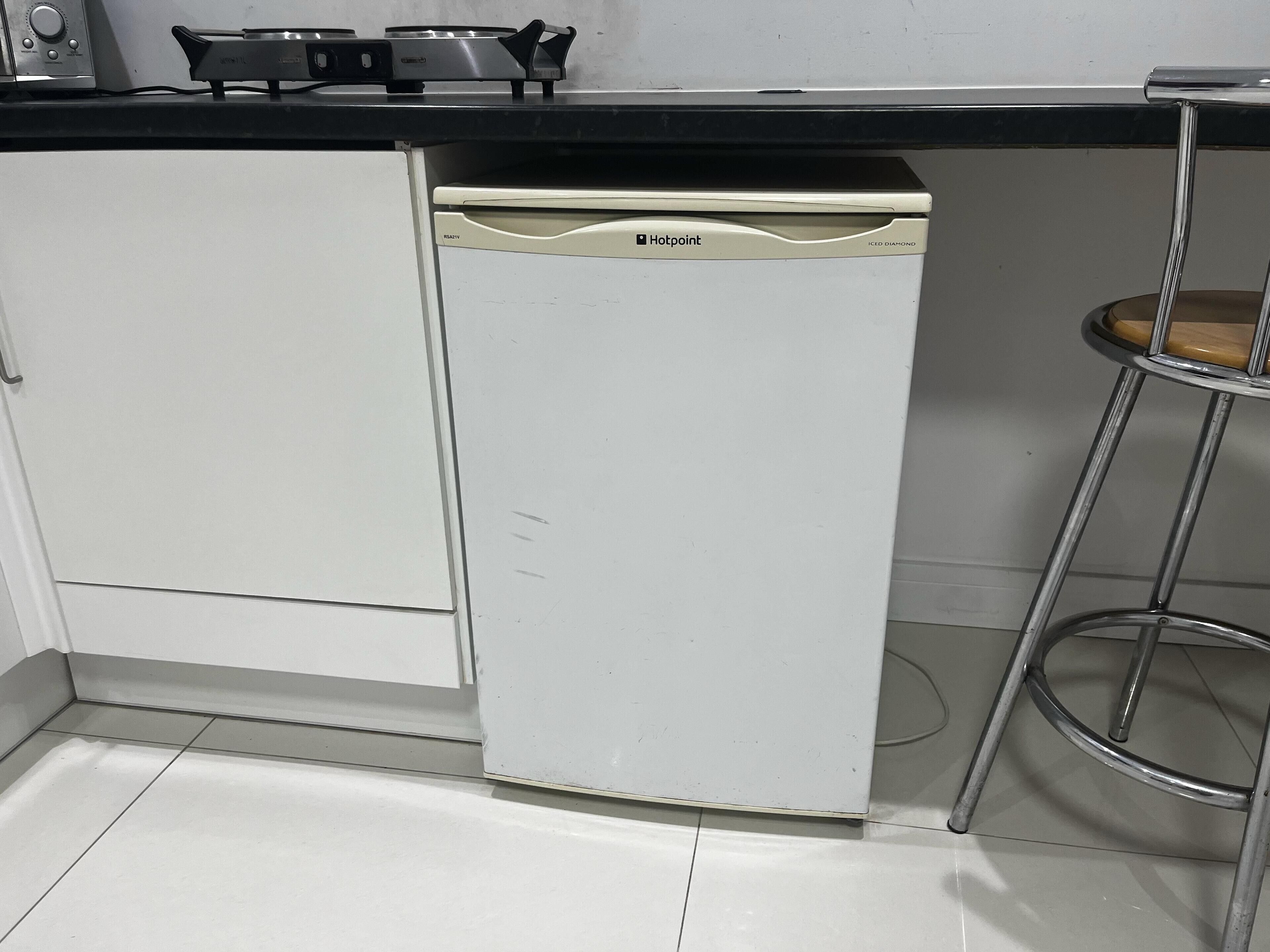 Una cocina compacta con lavavajillas, estufa y un taburete metálico.