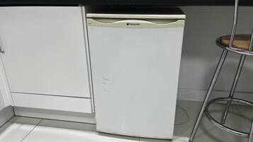 Una cocina compacta con lavavajillas, estufa y un taburete metálico.